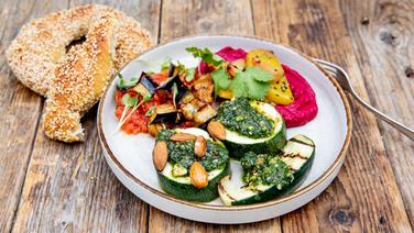 A plate of beetroot hummus, aubergines in tomato sauce and zucchini with pesto.  Next to it is a sesame ring © NDR Photo: Claudia Timmann