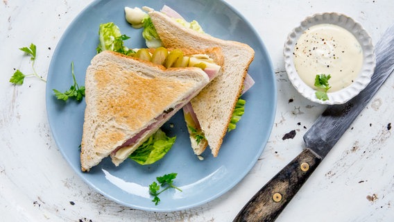 Two cheese and ham sandwiches on a plate with honey mustard dip.  Next to it is a wooden knife.  © NDR Photo: Claudia Timmann