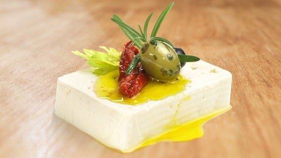 Ein Stück Feta mit Olivenöl beträufelt und mit Oliven, Kräutern und einer getrockneten Tomate dekoriert. © fotolia Foto: ExQuisine