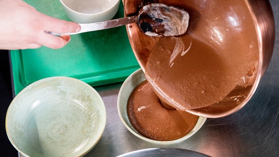 Ein Koch füllt fertige Schokoladen-Mousse in eine Porzellanschüssel. © NDR Foto: Claudia Timmann