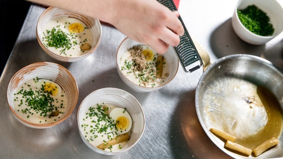 Ein Koch reibt Trüffel über eine Schale mit Schwarzwurzel-Cremesuppe. © NDR Foto: Claudia Timmann