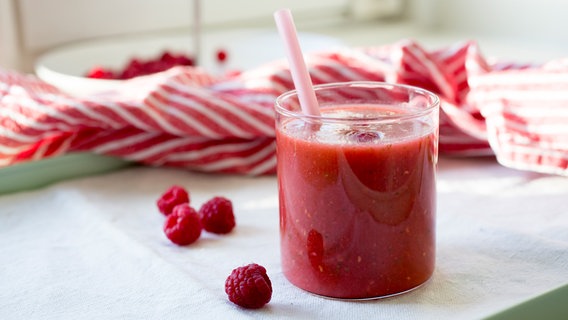 Raspberry, peach and lettuce smoothie in a glass and raspberries on the table.  © NDR Photo: Claudia Timmann