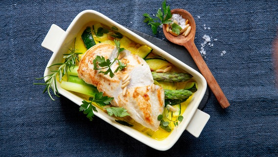 A casserole with asparagus and zucchini casserole with chicken fillet is on a table.  © NDR Photo: Claudia Timmann