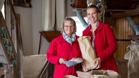 Theresa Baumgärtner und Annette Bösch stehen mit einer Tüte Mehl in einer Mühle. © NDR Foto: Claudia Timmann