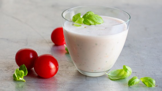 Tomaten-Buttermilch-Shake in einem Glas. Daneben liegen Tomaten und Basilikumblätter. © NDR Foto: Claudia Timmann