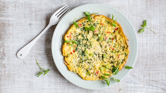 A plate of scrambled eggs with tomato and zucchini sits on a table.  © NDR Photo: Claudia Timmann