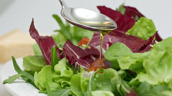 Oil is poured over mixed leaf salad on a plate with a spoon.  © fotolia Photo: gudrun