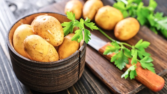 Potatoes in a bowl, behind them a cutting board and a knife.  © Color photo: Y. Haivoronska