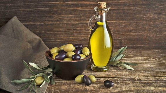 Olivenöl in einer Glasflasche sowie frische Oliven stehen auf einem Holztisch. © imago images / Panthermedia Foto: zidi
