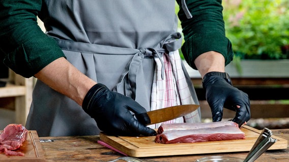 Ein Koch pariert Rehrückenfilets, die auf einem Küchenbrett liegen. © NDR Foto: Claudia Timmann
