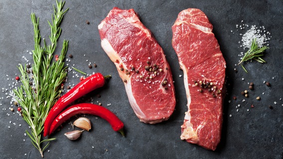 Zwei rohe Rindersteaks mit Rosmarinzweigen, Chilis und Gewürzen auf einem Schieferbrett. © fotolia Foto: Evgeny Karandaev