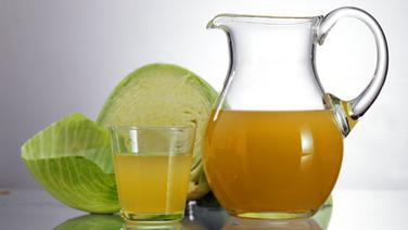 Auf einem Tisch stehen Sauerkrautsaft in einem Glas und in einer Karaffe vor einem Stück Weißkohl. © picture-alliance 
