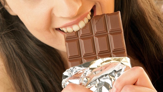 Eine junge Frau beißt in eine Tafel Schokolade. © Fotolia Foto: studiovespa