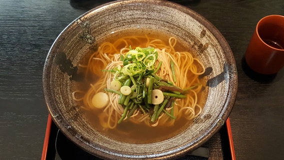 Eine japanische Suppe mit Sobanudeln und Gemüse in einer dunklen Schale serviert. © NDR Foto: Kathrin Weber