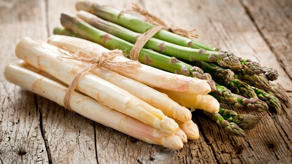 A bunch of white and a bunch of green asparagus lie on a wooden table.  © Fotolia/karep 