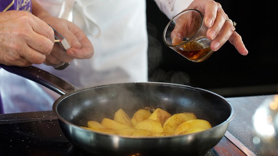 Calvados wird in eine Pfanne mit Apfelspalten gegossen © NDR Foto: Claudia Timmann