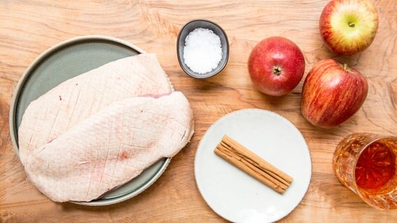 Auf einem Küchenbrett liegen zwei Entenbrüste, Äpfeln und Zimtstangen. © NDR Foto: Claudia Timmann
