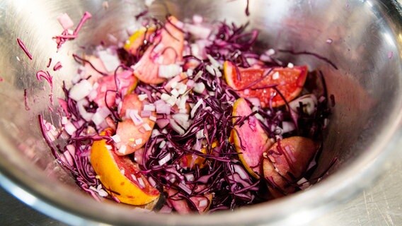 Klein geschnittener Rotkohl wird mit kleingeschnittenen Schalotten, Äpfeln und Orangen in einem Topf mariniert. © NDR Foto: Claudia Timmann