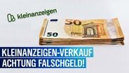 Auf einer weißen Fläche liegt ein Bündel 50 Euro Scheine. Daneben ist das Logo von Kleinanzeigen zu sehen. Der Text lautet: Kleinanzeigen-Verkauf - Achtung Falschgeld! © Daniel Kubirski Foto: Daniel Kubirski