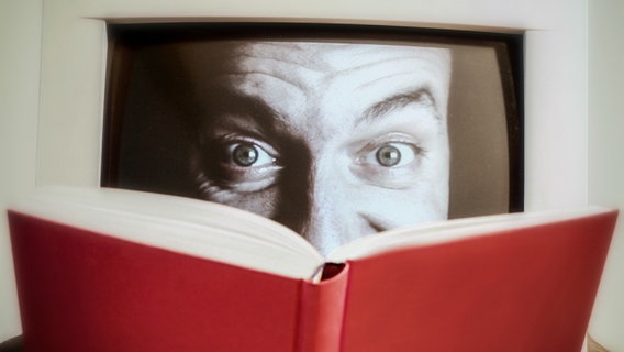 Ein Gesicht auf einem Monitor schaut mit aufgerissenen Augen über ein Buch. © photocase Foto: Spacejunkie