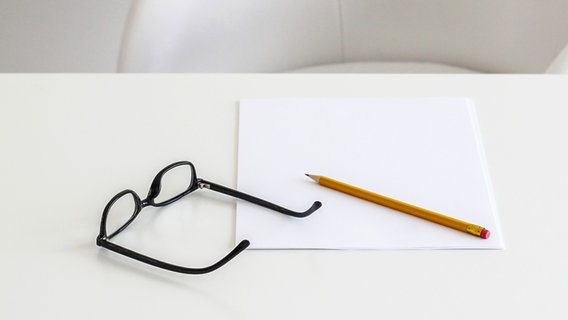 Auf einem leeren Schreibtisch liegt ein Bleistift, eine Brille und ein leeres Blatt Papier © photocase Foto: marshi