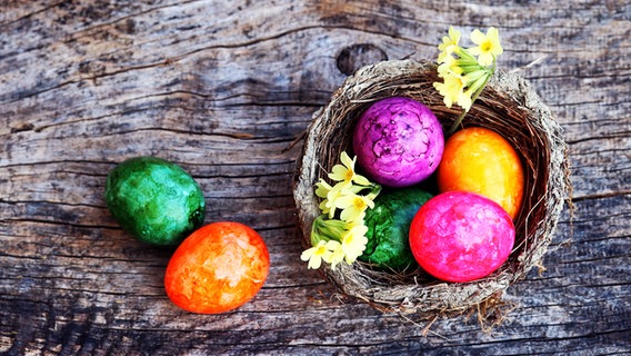 Bunte Ostereier liegen in einem Körbchen und auf einem Holztisch. © colourbox Foto: Astrid Gast