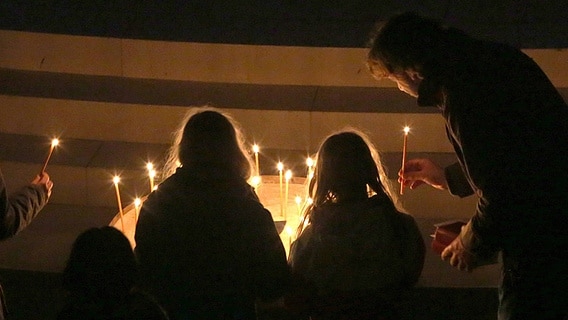 Mehrere Menschen stellen in einer dunklen Kirche Kerzen auf. © imago images / epd 