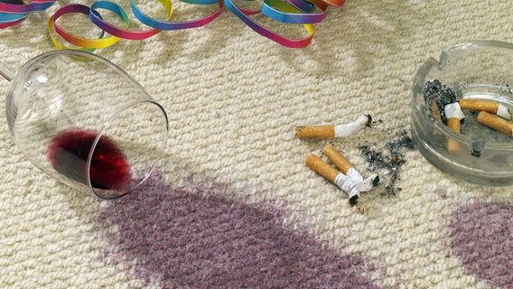 Auf einem Teppich liegen ein ausgekipptes Glas Rotwein und Zigarettenkippen © Fotolia Foto: akf