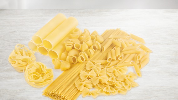 Diverse Pastasorten wie Spaghetti, Penne, Farfalle und Fettuccine liegen auf einem Küchentisch. © fotolia.com Foto: roman_baiadin