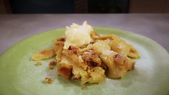 Ein zerkleinerter Pfannkuchen mit Stollen liegt auf einem grünen Teller. © NDR 