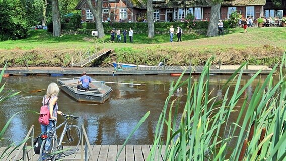 Ein Fährmann holt eine Frau mit ihrem Fahrrad ab, um sie per Boot über die Wümme in das Bremer Blockand überzusetzen. © dpa / picture alliance Foto: Ingo Wagner