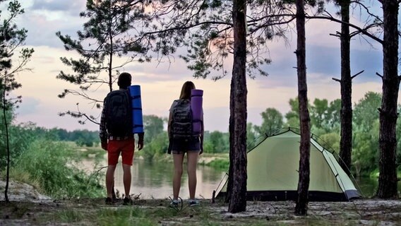 Zwei  Menschen stehen an einem See, neben ihnen ein Zelt. © Colourbox Foto: Ievgen Chabanov
