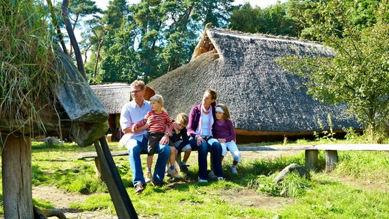 Eine Familie mit drei Kindern sitzt auf einem Holzbalken im Bronzezeithof in Uelsen © Grafschaft Bentheim Tourismus 