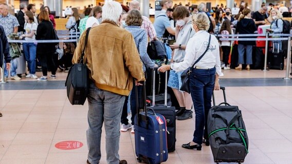 Reisende stehen mit Gepäck vor einem Check-In-Schalter am Hamburger Flughafen. © picture alliance/dpa Foto: Axel Heimken
