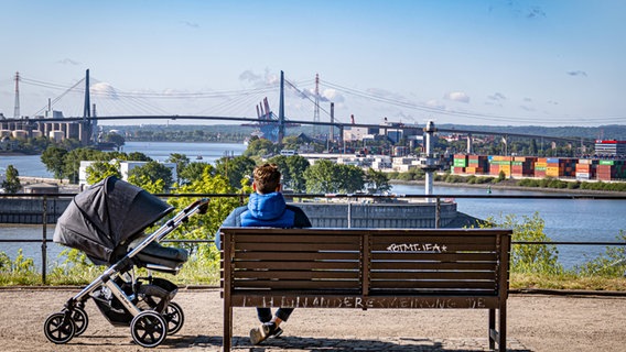 Ein Mann mit Kinderwagen sitzt auf einer Bank am Altonaer Balkon und schaut auf die Elbe und die Köhlbrandbrücke. © imago images Foto: Jürgen Ritter