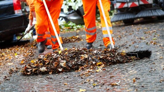 Mitarbeiter der Straßenreinigung kehren Laub zusammen. Mitarbeiter der Straßenreinigung kehren Laub zusammen. © dpa Bildfunk Foto: Christian Charisius/dpa