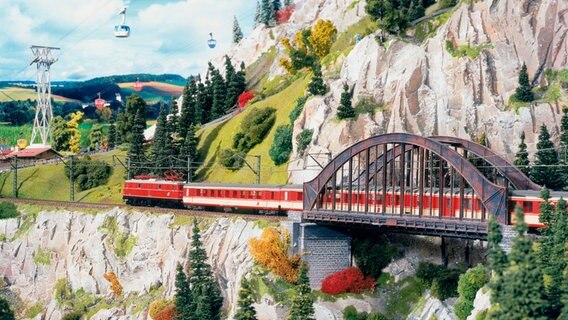 Ein Zug fährt in einer Berglandschaft des Miniatur Wunderlandes über eine Eisenbrücke © Miniatur Wunderland 
