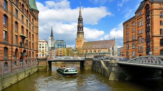 Eine Barkasse fährt auf einem Fleet durch die Hamburger Speicherstadt, im Hintergrund die Katharinenkirche. © fotolia Foto: kameraauge