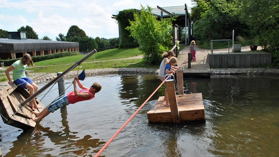 Auf dem Wasserspielplatz im Kiekeberg-Museum fahren Kinder mit einem  Floß.  