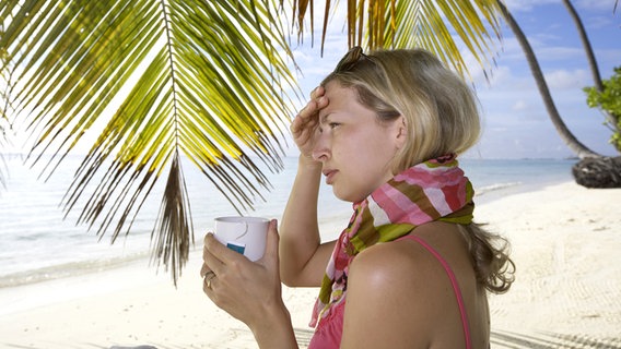Frau mit Halstuch am Strand, hält einen Becher Tee in der Hand. © Fotolia Foto: epics