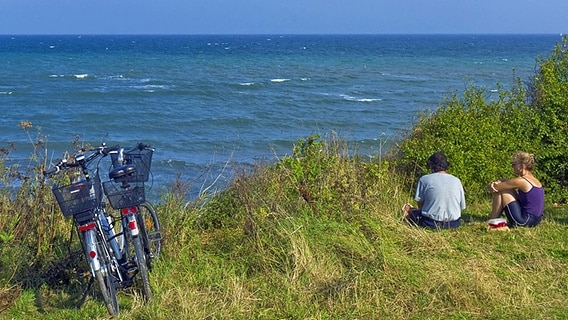 Zwei Radfahrer sitzen neben ihren Rädern an der Ostseeküste. © imago/blickwinkel 