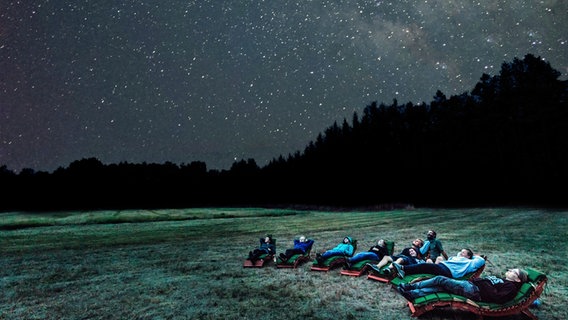 Menschen liegen bei Nacht auf einer Wiese im Naturpark Nossentiner/Schwinzer Heide und beobachten die Sterne. © TMV Foto: Markus Kirchgessner