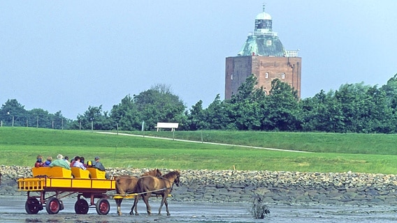 Ein gelber Wattwagen vor dem Leuchtturm der Insel Neuwerk © imago/blickwinkel 