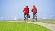Zwei Radfahrer fahren auf einem Deich an der Nordsee bei Dangast am Jadebusen, im Hintergrund mehrere Windräder. © picture-alliance/ dpa Foto: Wolfram Steinberg
