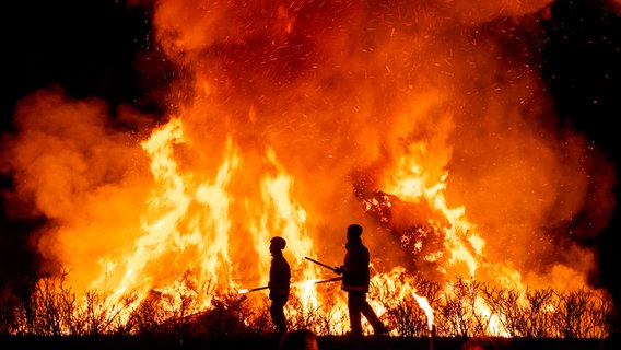 Zwei Besucher gehen beim Biikebrennen auf Sylt am Feuer entlang. © picture alliance/dpa Foto: Daniel Bockwoldt