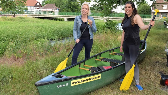 Die Reporterinnen Vanessa Kossen und Britta von Lucke stehen auf einer Wiese vor einem Kanu. © NDR/dmfilm Foto: Michael Bahlo