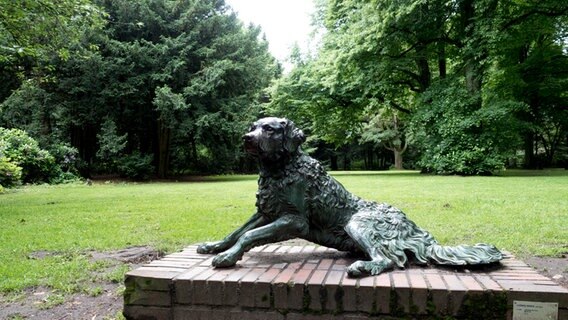 Eine Hundefigur aus Bronze liegt auf einem Sockel im Hamburger Stadtpark.  Foto: Anja Deuble