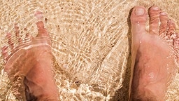 Zwei nackte Füße stehen im flachen Wasser auf einem Sandboden. © Colourbox Foto: #98688