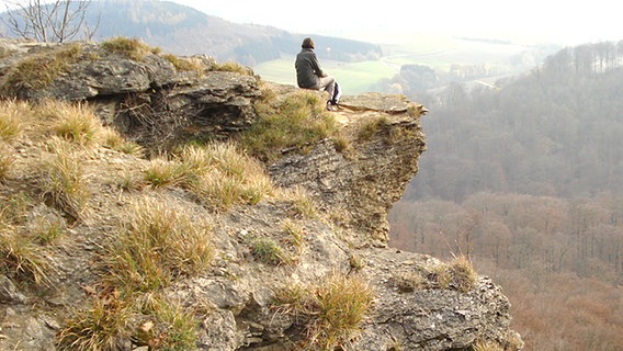 Ein Wanderer sitzt auf einer Klippe am Hohenstein im Süntel und schaut ins Tal. © NDR Foto: Axel Franz