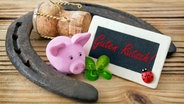 Glücksschweinchen, Hufeisen, Sektkorken, Kleeblatt und ein Schild mit der Aufschrift "Guten Rutsch!" auf einem Holztisch. © Fotolia Foto: PhotoSG - stock.adobe.com